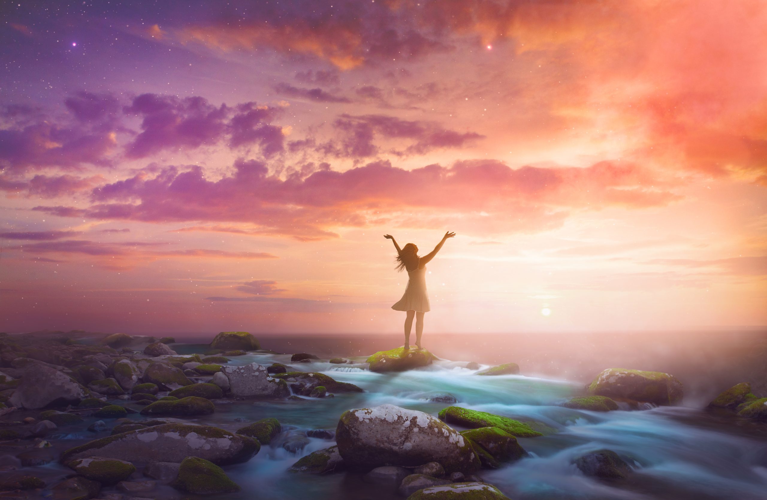 A woman lifts her arms in praise at sunrise